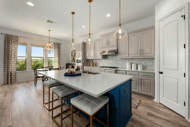 kitchen with tasteful backsplash, visible vents, light wood-style flooring, under cabinet range hood, and a sink