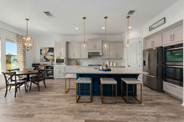 kitchen featuring under cabinet range hood, stainless steel appliances, visible vents, light countertops, and tasteful backsplash