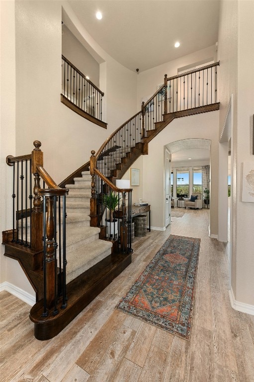 foyer with a high ceiling, baseboards, arched walkways, and wood finished floors