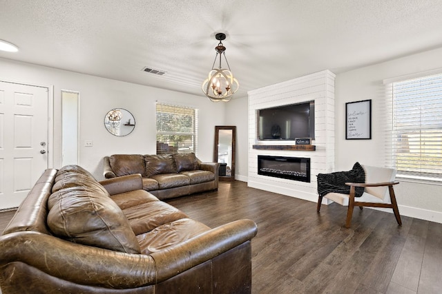 living room featuring dark wood-style flooring, visible vents, a large fireplace, a textured ceiling, and a chandelier