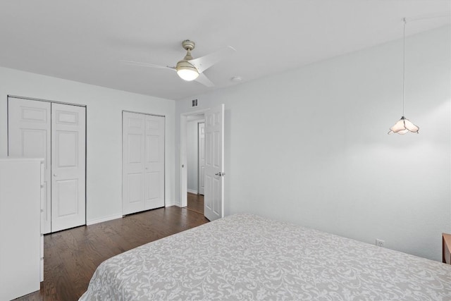 bedroom with wood finished floors, visible vents, baseboards, a ceiling fan, and two closets