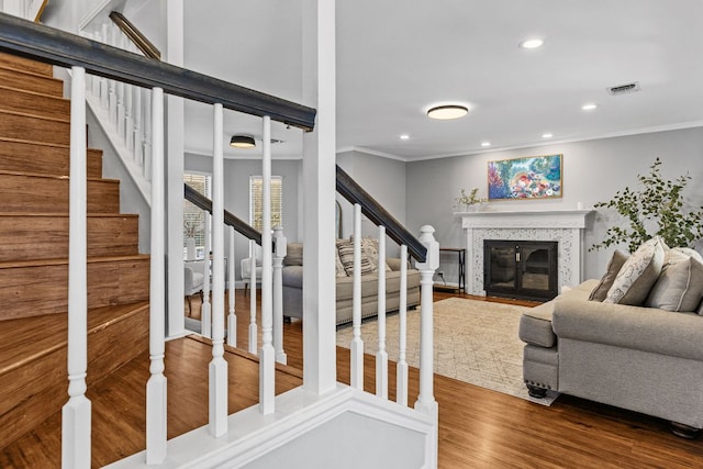 living room with wood finished floors, a fireplace with flush hearth, visible vents, ornamental molding, and stairway