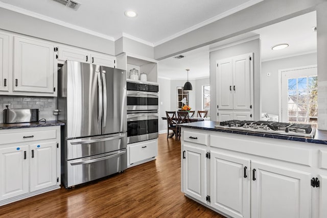 kitchen with stainless steel appliances, dark countertops, white cabinetry, and crown molding