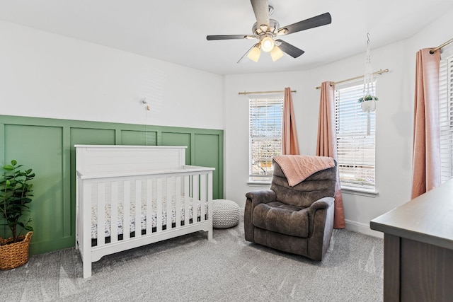 carpeted bedroom with a nursery area, a decorative wall, and ceiling fan