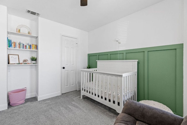 carpeted bedroom with a nursery area, visible vents, a decorative wall, and ceiling fan