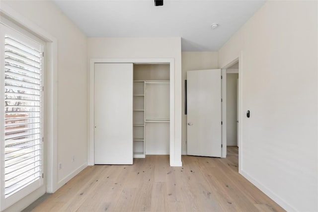 unfurnished bedroom featuring light wood-type flooring, multiple windows, baseboards, and a closet