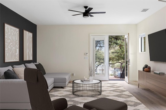 living area with ceiling fan, wood finished floors, visible vents, and baseboards