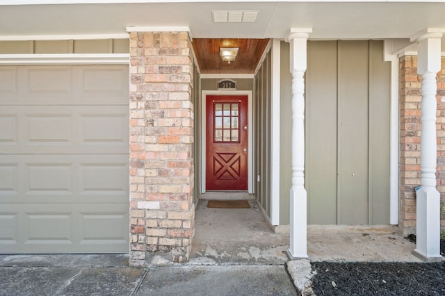 entrance to property featuring a garage, brick siding, and visible vents