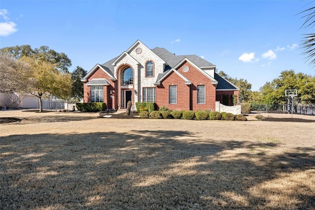 view of front of home featuring brick siding, stone siding, a front yard, and fence