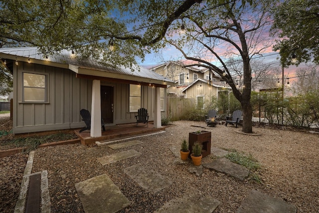 back of house at dusk featuring metal roof, board and batten siding, an outdoor structure, and fence