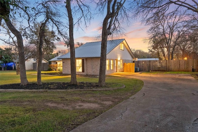 view of front of property featuring metal roof, brick siding, fence, a lawn, and curved driveway