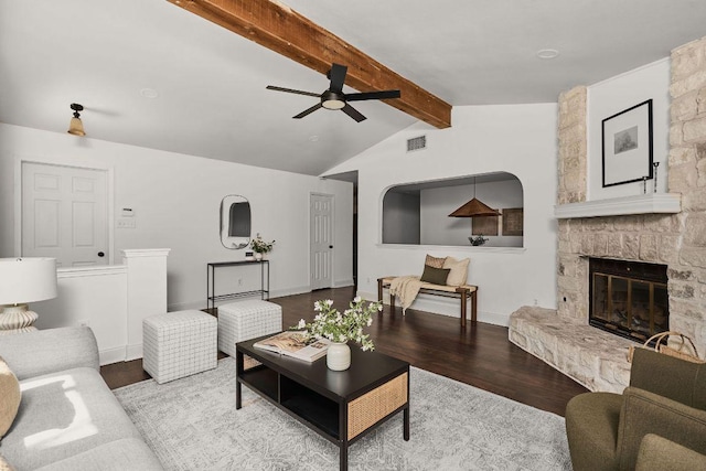 living area with visible vents, lofted ceiling with beams, a stone fireplace, wood finished floors, and baseboards