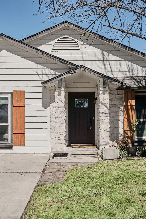 doorway to property with stone siding and a lawn