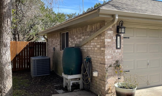 view of side of property with a garage, a shingled roof, fence, cooling unit, and brick siding