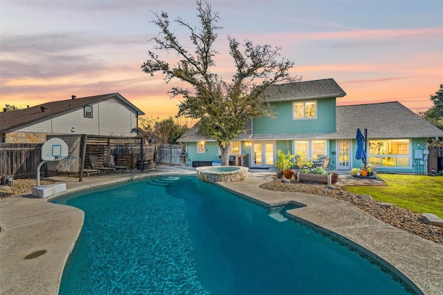 pool at dusk with a lawn, a patio, a fenced backyard, french doors, and a pool with connected hot tub