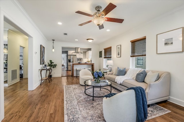 living room with baseboards, wood finished floors, visible vents, and crown molding