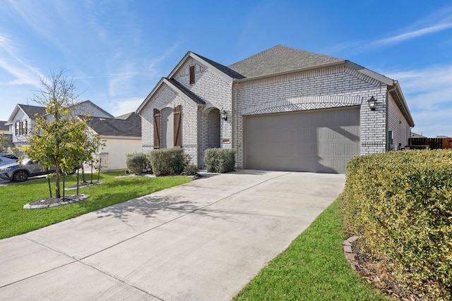 french country inspired facade with a garage, a shingled roof, concrete driveway, a front lawn, and brick siding