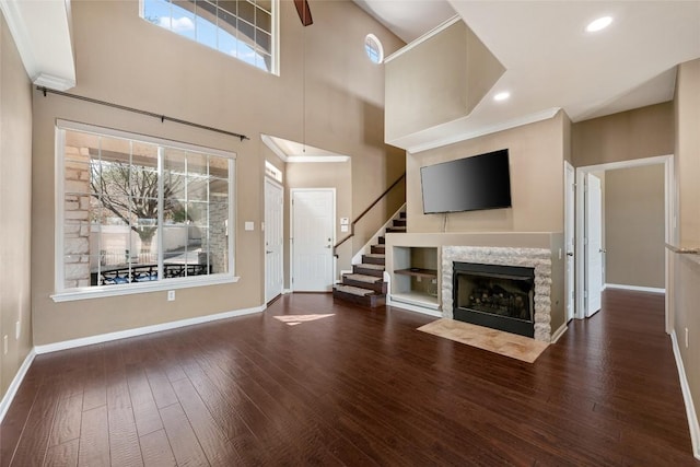 unfurnished living room with dark wood-type flooring, a fireplace with flush hearth, ornamental molding, baseboards, and stairs