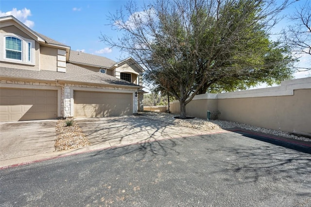 view of side of home featuring driveway, stucco siding, fence, and roof with shingles