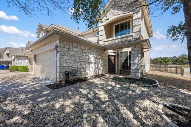 view of front of house featuring stone siding, concrete driveway, an attached garage, and fence