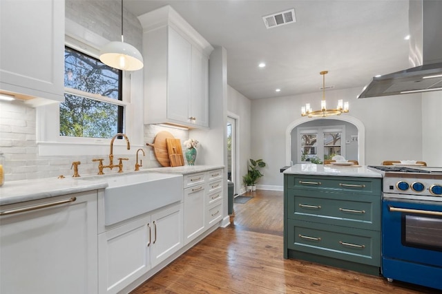 kitchen featuring a sink, visible vents, white cabinets, wall chimney range hood, and stainless steel range with gas stovetop