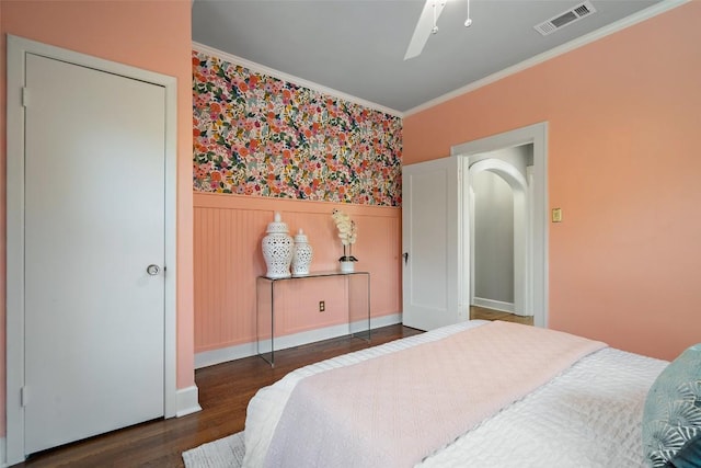 bedroom with ceiling fan, a wainscoted wall, wood finished floors, visible vents, and ornamental molding