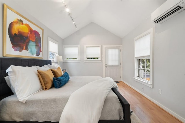 bedroom with lofted ceiling, baseboards, light wood-style floors, an AC wall unit, and track lighting