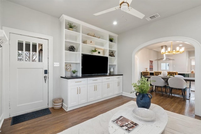 living area with arched walkways, visible vents, dark wood finished floors, and ceiling fan with notable chandelier