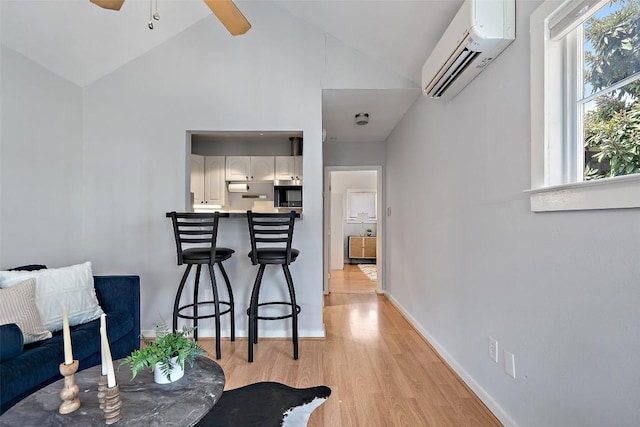 interior space featuring high vaulted ceiling, a ceiling fan, baseboards, a wall mounted AC, and light wood finished floors