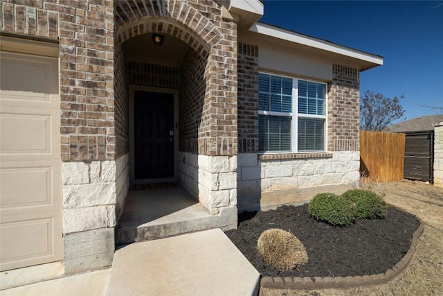 property entrance featuring an attached garage, fence, and brick siding