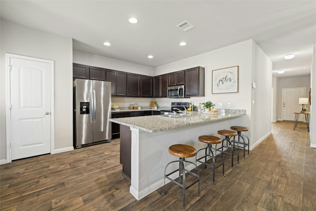 kitchen with a breakfast bar area, stainless steel appliances, dark wood-type flooring, visible vents, and dark brown cabinets