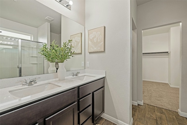 bathroom featuring double vanity, wood finished floors, a stall shower, and a sink