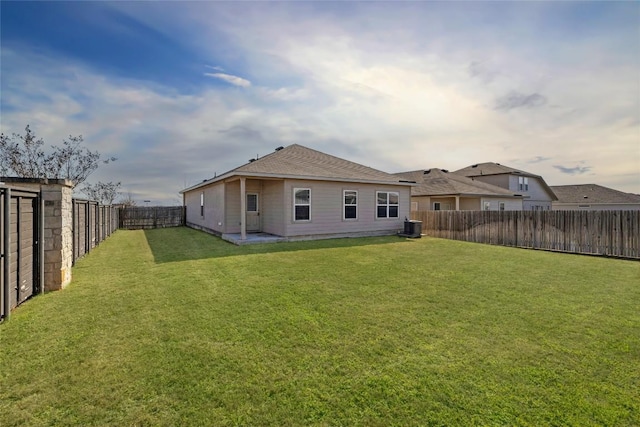 rear view of property with a fenced backyard, a shingled roof, central AC unit, and a lawn