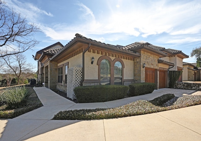 view of front of house with stone siding, driveway, an attached garage, and a tiled roof