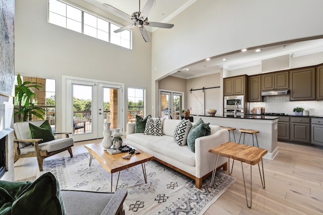 living area with a barn door, arched walkways, light wood-style flooring, crown molding, and french doors