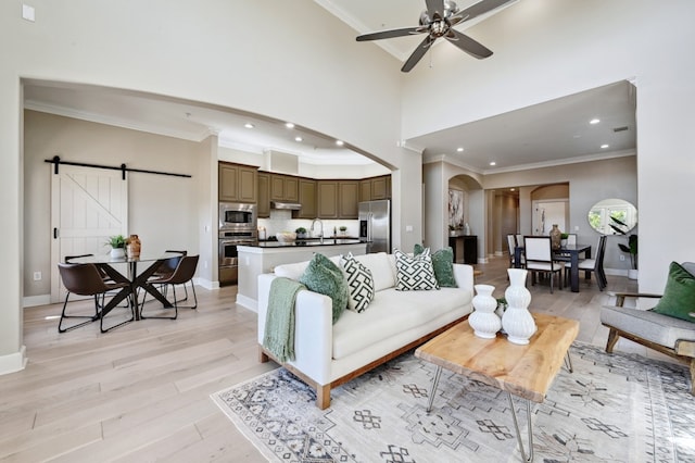 living room featuring arched walkways, a barn door, a high ceiling, and light wood-style floors