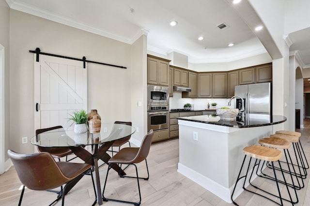 kitchen with a barn door, visible vents, appliances with stainless steel finishes, ornamental molding, and under cabinet range hood