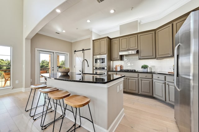 kitchen with a barn door, decorative backsplash, appliances with stainless steel finishes, under cabinet range hood, and a sink