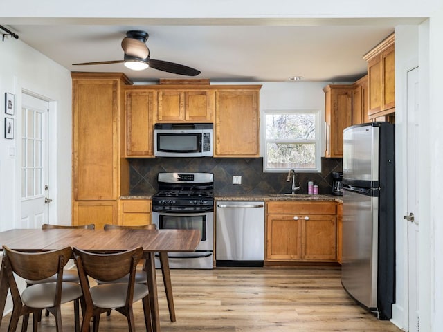 kitchen featuring stainless steel appliances, a sink, light wood-style floors, brown cabinets, and decorative backsplash