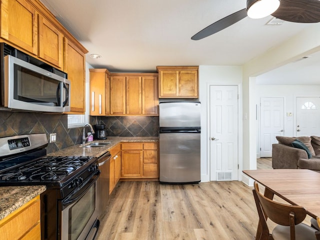 kitchen with brown cabinets, stainless steel appliances, visible vents, light wood-style flooring, and a sink