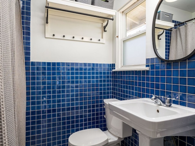 bathroom featuring a wainscoted wall, tile walls, a shower with shower curtain, toilet, and a sink