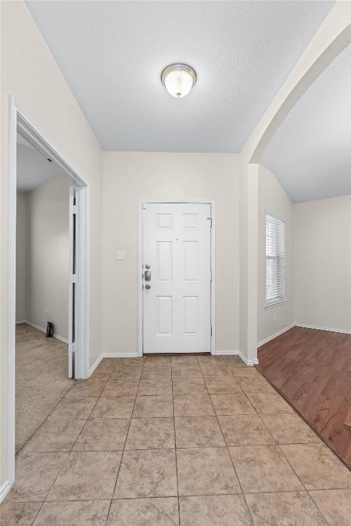 foyer entrance featuring arched walkways, light tile patterned flooring, a textured ceiling, and baseboards