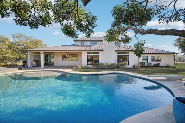 back of house with metal roof, a standing seam roof, a patio area, and an outdoor pool