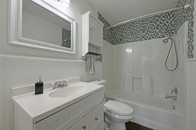 full bathroom with a textured ceiling,  shower combination, wainscoting, and toilet