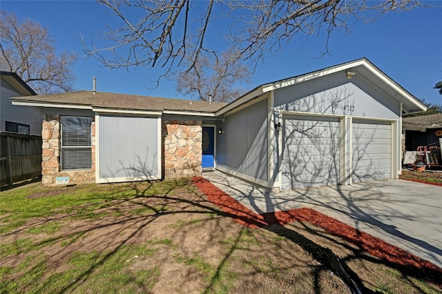 view of front of home with driveway, stone siding, an attached garage, and fence