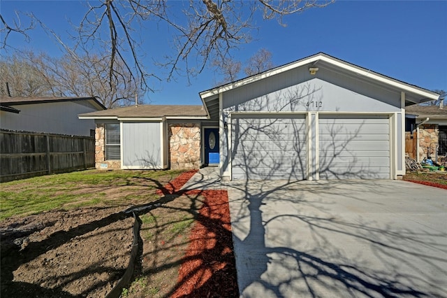 exterior space with stone siding, an attached garage, fence, and driveway