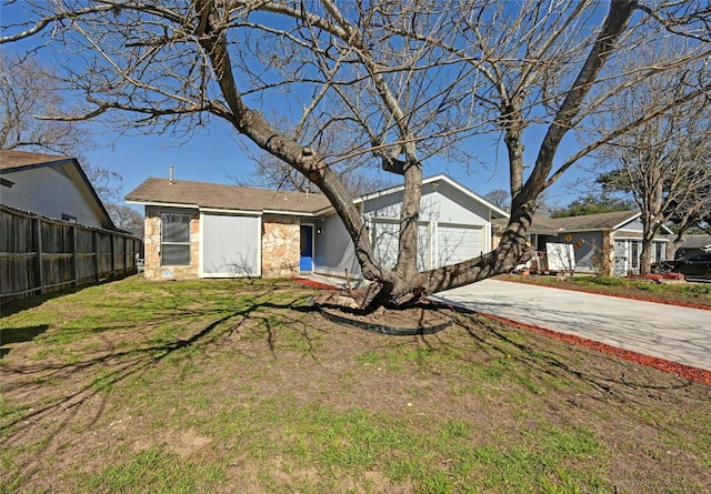 view of front facade with concrete driveway, stone siding, an attached garage, fence, and a front lawn