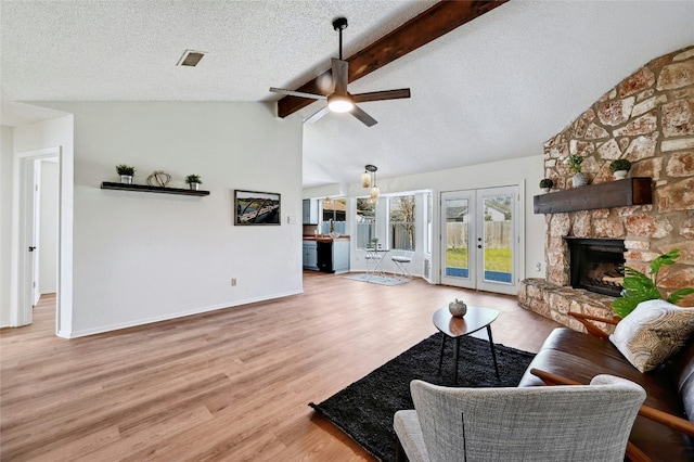 living room featuring visible vents, french doors, wood finished floors, vaulted ceiling with beams, and a stone fireplace