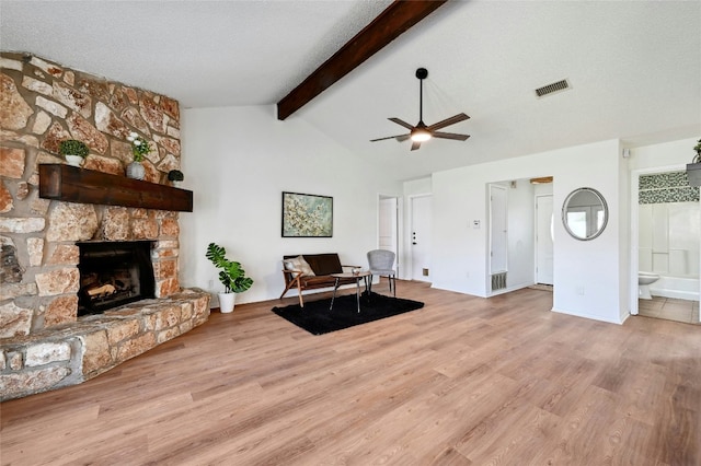 living area featuring lofted ceiling with beams, a stone fireplace, a textured ceiling, and wood finished floors