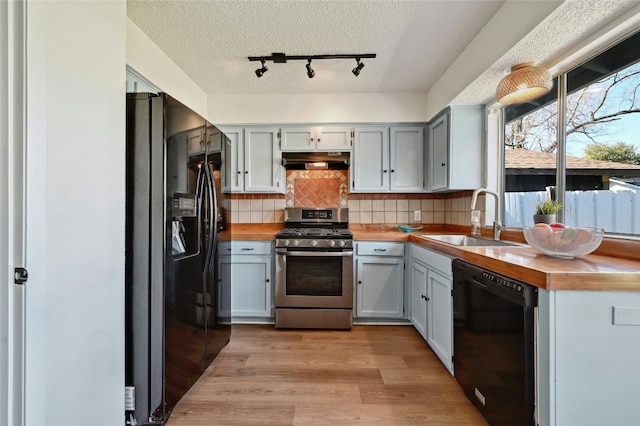 kitchen featuring black appliances, under cabinet range hood, a sink, and butcher block countertops